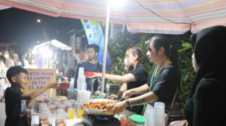Seorang penjual sedang menggoreng makanan di sebuah stand makanan di Bazar Kuliner Kampoeng Cungking. Terlihat beberapa orang pengunjung yang antusias mendekat ke stand tersebut.