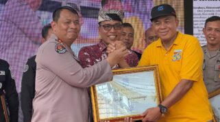 Seorang perwakilan Polresta Banyuwangi sedang menerima penghargaan berupa piagam dari seorang perwakilan Harian Memorandum. Kedua pria tersebut sedang berjabat tangan.