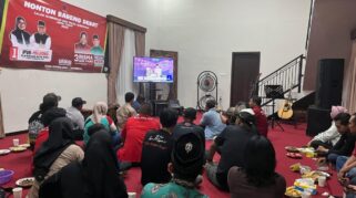 Sejumlah orang sedang menonton televisi di sebuah ruangan. Suasana terlihat ramai dan hangat.