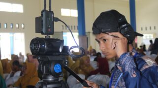 Seorang siswa SMK Muhammadiyah 8 Siliragung sedang meliput acara dengan kamera video profesional.