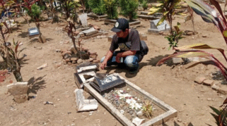 Seorang pria memeriksa nisan makam yang rusak dan berserakan.